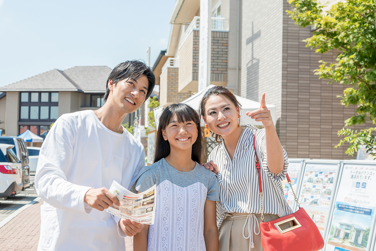 モデルハウスの前で見学を楽しみにしている家族。両親と子供が笑顔で会話