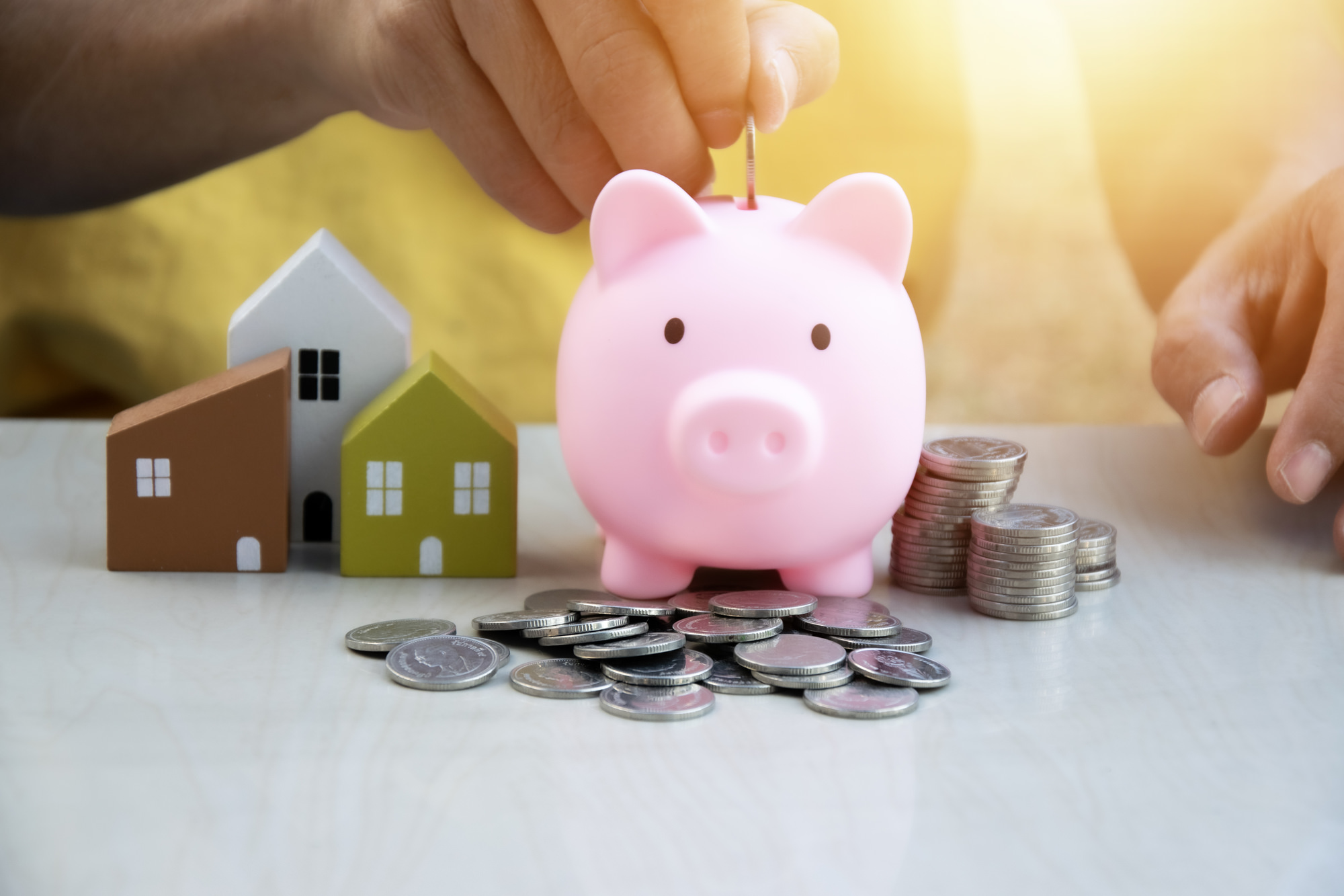 ピンクのブタの貯金箱と積み上げられた硬貨。住宅ローンと資産形成の関係を示すビジュアル